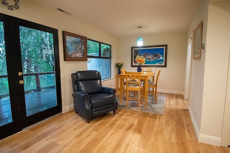 Dining room with picture windows offering sunlit forest view while dining.