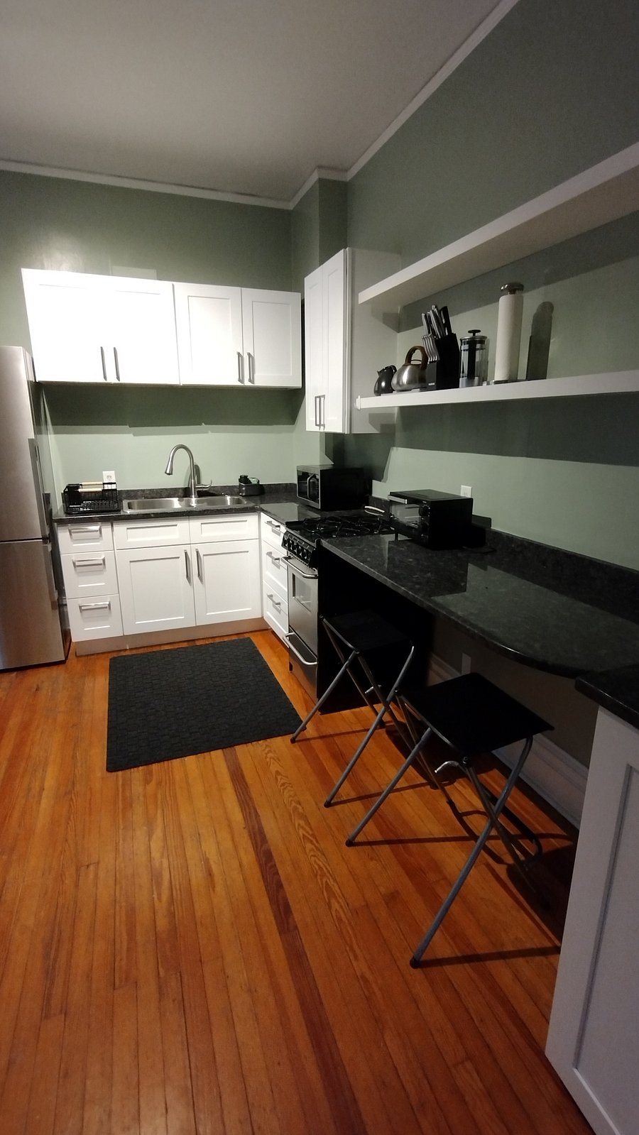 Kitchen sink, stove and granite counter top. The counter top has two high top stools for working on the computer or just hanging out.