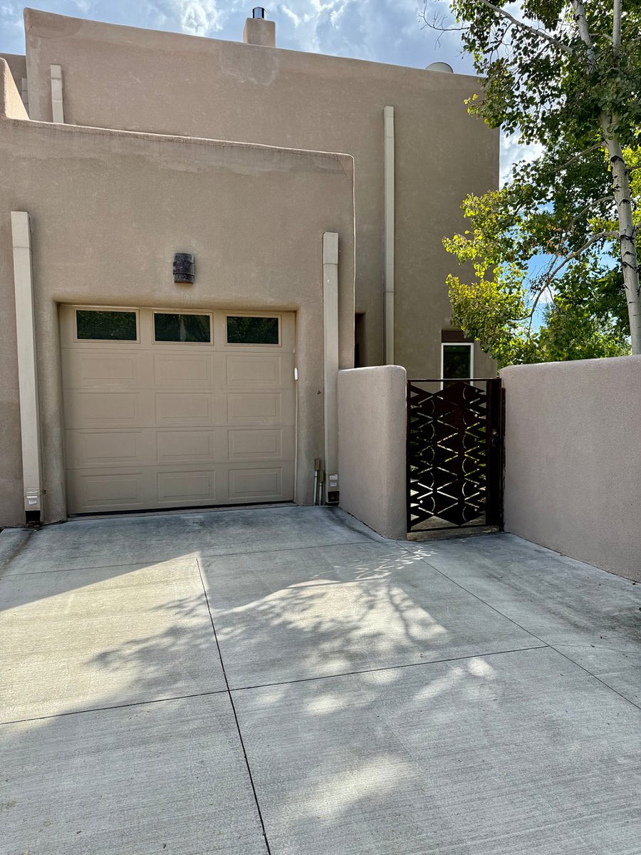 Front view of this lovely condo, showing garage door to the single-car garage, the additional driveway pad parking space, and the custom-made entry gate.