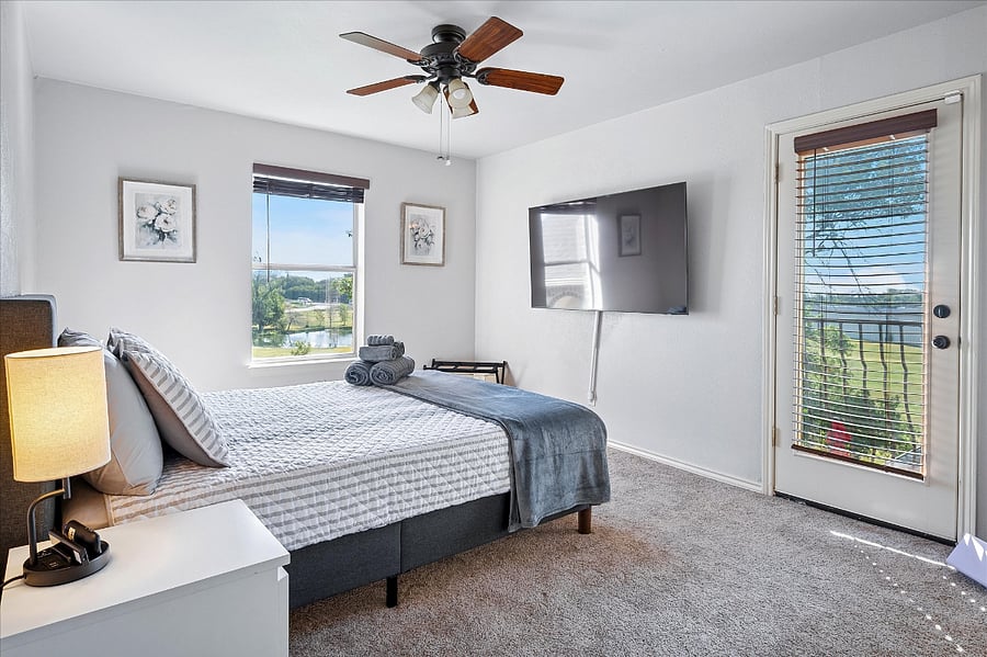 Relaxing upstairs bedroom with a queen bed, wall-mounted TV, attached full bathroom, and peaceful pond views