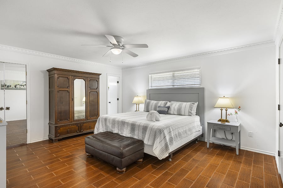 Master bedroom with king bed, TV, ceiling fan, two walk in closets, dresser, wardrobe, and ensuite bathroom.