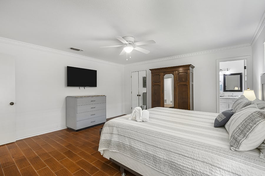 Master bedroom with king bed, TV, ceiling fan, two walk in closets, dresser, wardrobe, and ensuite bathroom.