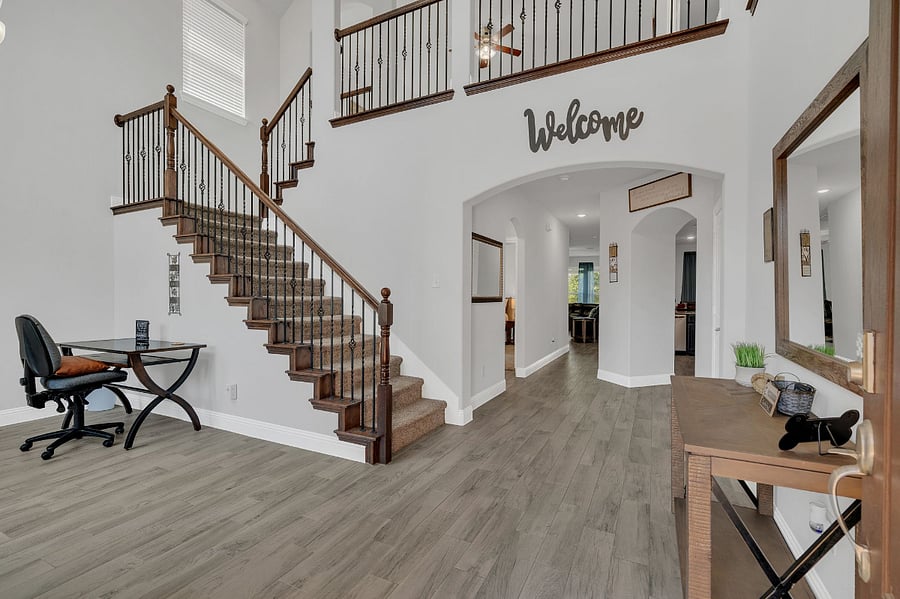 Inviting entry with soaring ceilings, wrought iron staircase, and warm natural light. Features a welcoming console table and dedicated workspace, opening to the main living areas beyond.