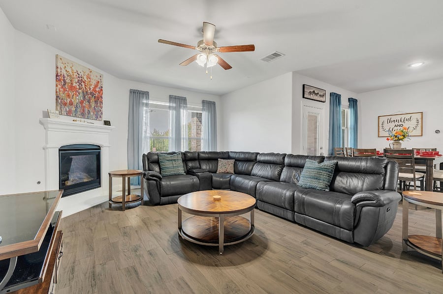 Living room with a sectional leather sofa and power recline, with direct vent gas fireplace (use switch on wall to light ceramic logs), large Smart TV, side tables, center table, open concept with kitchen, dining, and backyard/patio with lake views. Bright, comfortable seating, and direct sightlines to the kitchen and backyard.