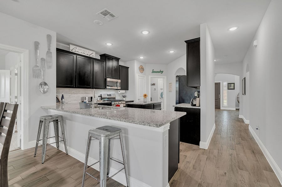 Open-concept kitchen with granite counters, stainless appliances, gas range, large island, and bar seating overlooking the living areas.