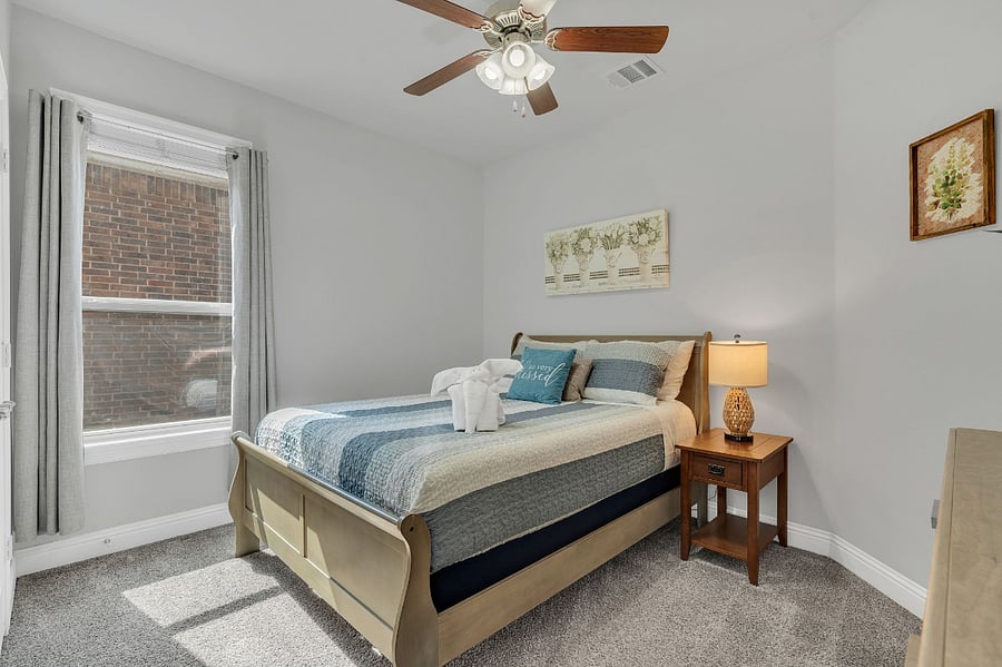 Second downstairs bedroom with queen bed, dresser, nightstand, and ceiling fan. Located near a full bathroom with a step-in shower, making it convenient for guests with limited mobility or those who prefer easy access.