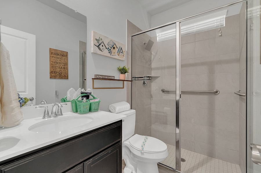 Second downstairs bedroom with queen bed, dresser, nightstand, and ceiling fan. Located near a full bathroom with a step-in shower, making it convenient for guests with limited mobility or those who prefer easy access.