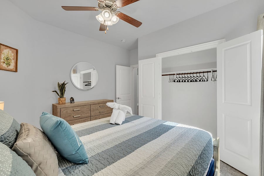 Second downstairs bedroom with queen bed, dresser, nightstand, and ceiling fan. Located near a full bathroom with a step-in shower, making it convenient for guests with limited mobility or those who prefer easy access.