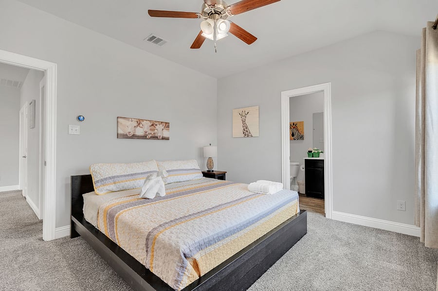 Upstairs bedroom with king bed, ensuite bathroom (tub/shower combo), and walk-in closet (not pictured). Bright natural light and plenty of space for comfort.
