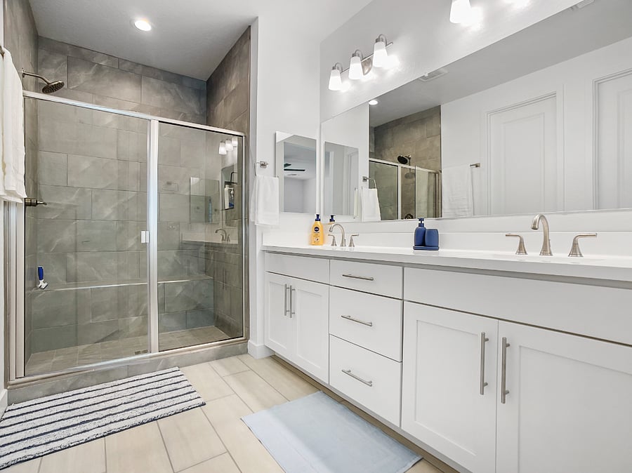 Full master bathroom featuring a walk-in, stand up shower, double vanity sinks, and an adjoining walk-in closet.