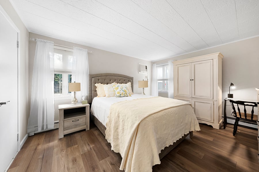 Another view of the larger queen bedroom, showing its dedicated workstation, wardrobe, wall air conditioner, and room-darkening shades.