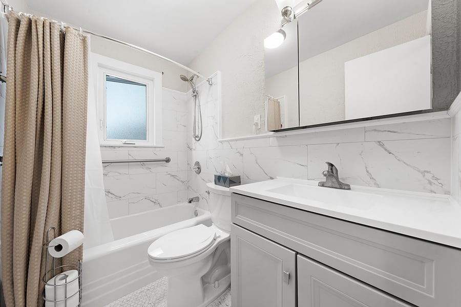 Newly remodeled hall bathroom with a tub/shower, tiled walls, safety grab bars, a vanity, and an exhaust fan.