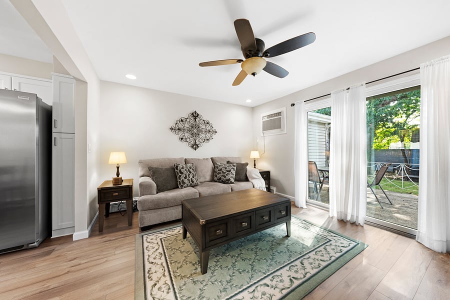 Bright furnished living room with comfortable seating and sliding glass doors opening directly onto the private back deck, with outdoor seating for four.