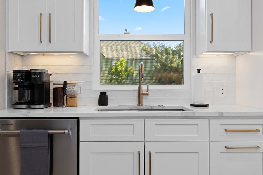Clean kitchen with Keurig coffee station, stainless steel dishwasher, and modern faucet. Ideal for short-term stays with daily convenience, bright natural light, and fully stocked essentials for remote work or vacation rentals.