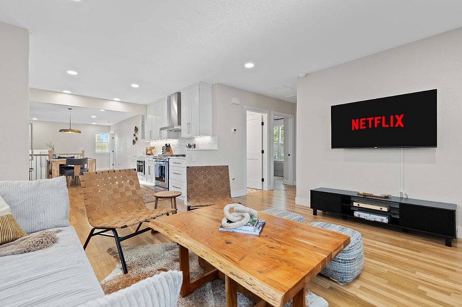 Open-concept living area with smart TV, clean modern kitchen, and natural wood finishes. Perfect for short-term stays with updated appliances, streaming setup, and spacious layout for remote work or group travel.