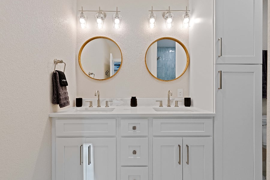 Spotless bathroom with double vanity, modern lighting, and gold-framed mirrors. Ideal for short-term stays with updated fixtures, clean design, and ample storage for extended or group bookings.