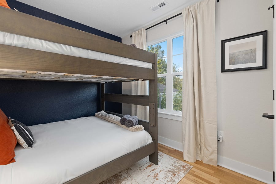 Clean bedroom with queen-size bunk beds, natural light, and modern accent wall. Ideal for short-term rentals hosting families or groups, offering stylish, functional, and cozy sleeping accommodations.