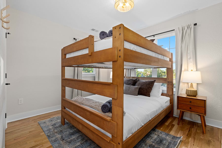 Clean bedroom with queen bunk beds, hardwood floors, and natural light. Ideal for short-term rentals accommodating families or groups with modern furnishings and cozy sleeping arrangements.