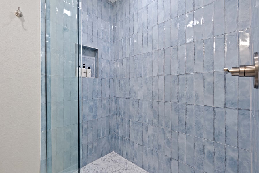 Walk-in shower with clean glass door, modern blue tile, and built-in niche. Ideal for short-term rentals with updated bathroom features and a spotless, spa-inspired design.