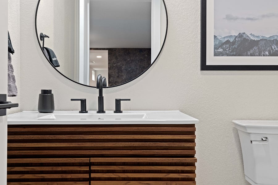 Modern bathroom with wood slat vanity, matte black fixtures, and round mirror. Clean and stylish design ideal for short-term rentals focused on updated amenities and boutique hotel feel.