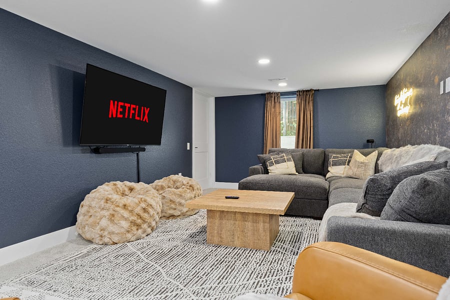 Entertainment-ready movie room featuring a mounted TV with streaming access, plush sectional, cozy bean bags, and stylish decor. Perfect for short-term rentals looking to offer guests a dedicated, comfortable movie night space.