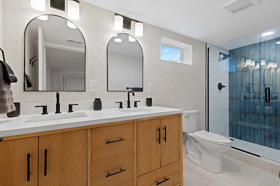 Contemporary bathroom with double vanity, matte black fixtures, and a walk-in glass shower with striking blue tile. A polished and functional space that enhances guest appeal in any short-term rental.