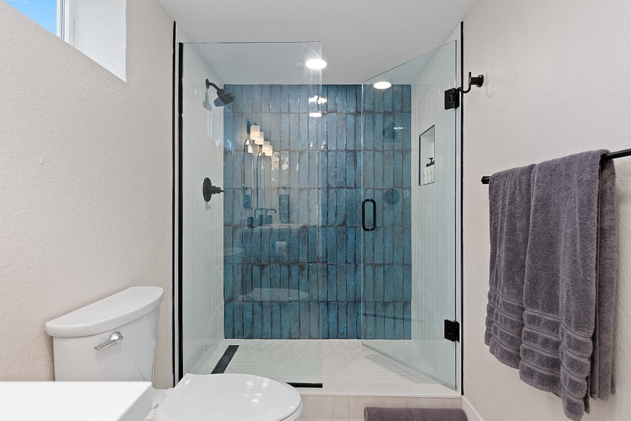 This walk-in shower features striking blue vertical tiles, sleek glass panels, and matte black hardware. The bold design brings a modern, spa-like feel to the bathroom.