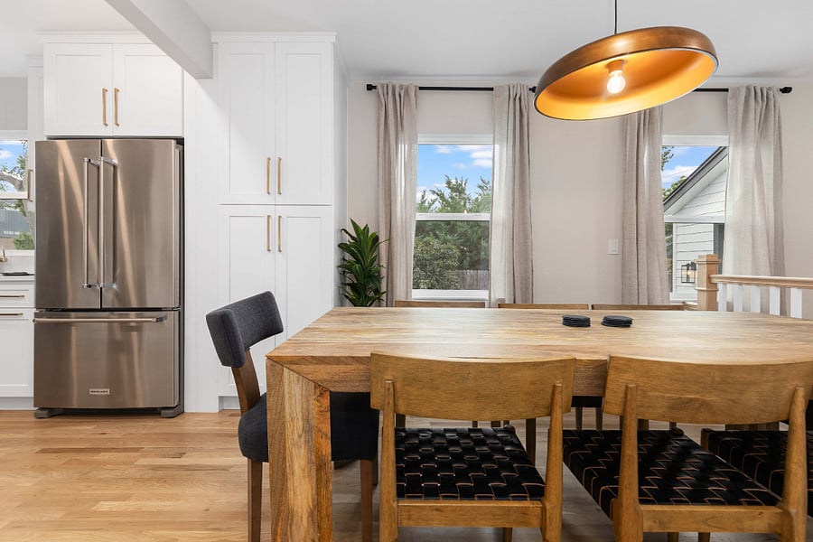 Modern dining area with natural wood table, sleek lighting, and stainless steel appliances. Clean and bright space ideal for short-term stays with updated kitchen, ample seating, and natural light for remote work or family meals.