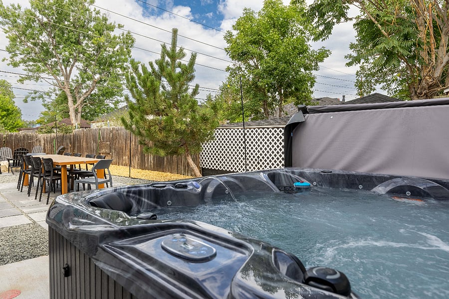 Private backyard with large hot tub, outdoor dining table, and seating area. Perfect for groups seeking a clean, secluded, and relaxing short-term rental with spa-style amenities and al fresco entertaining space.Entertainment-ready movie room featuring a mounted TV with streaming access, plush sectional, cozy bean bags, and stylish decor. Perfect for short-term rentals looking to offer guests a dedicated, comfortable movie night space.