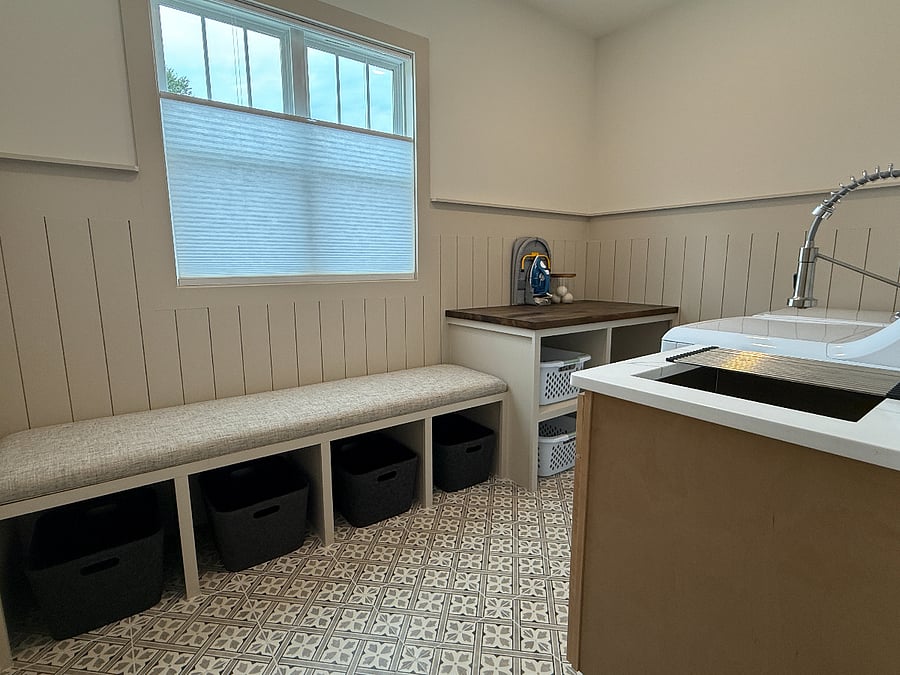 Laundry space complete with mudroom benching, wall pegs and folding table, washer, dryer and deep sink with hanging bar