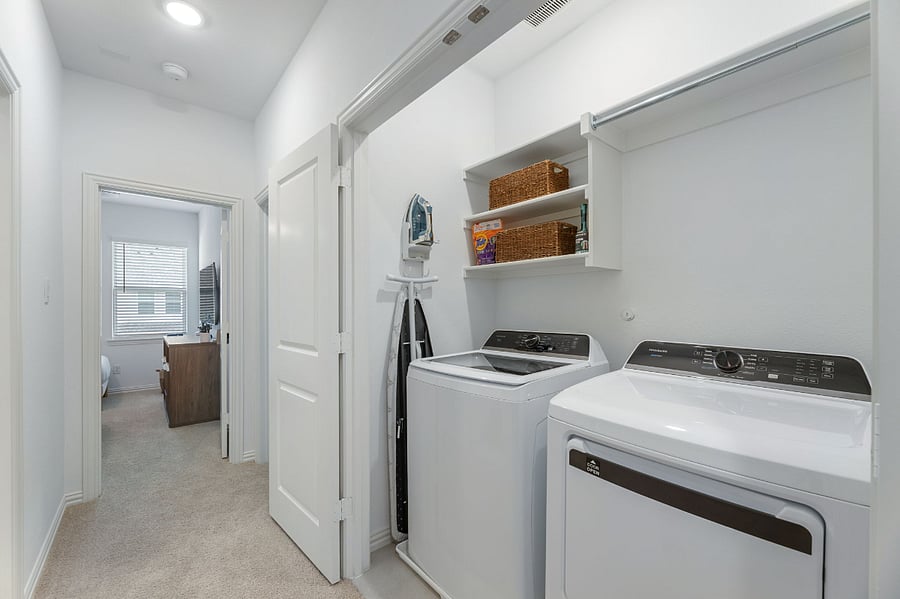 In home laundry area with new washer and dryer. Also includes an iron and ironing board.