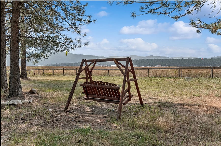 Backyard includes view of mountains, trees, large lawn, firepit, chicken coop, garden.