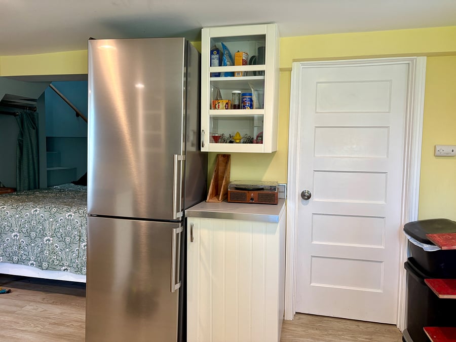 A new mid-size Forno refrigerator was installed in October. The door on the right leads to the bathroom. Recycling bins can be spotted stacked on the far left, next to a shoe rack.