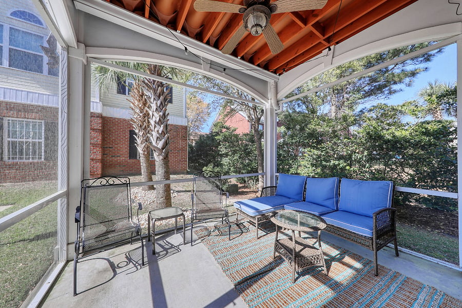 Outside the porch, there are trees and a brick building. The overall scene suggests a relaxing outdoor living space.