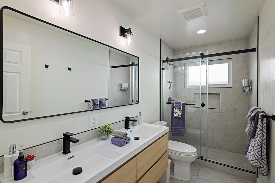 Sleek modern bathroom with double vanity, frameless glass shower, natural light, and stylish black & white decor.