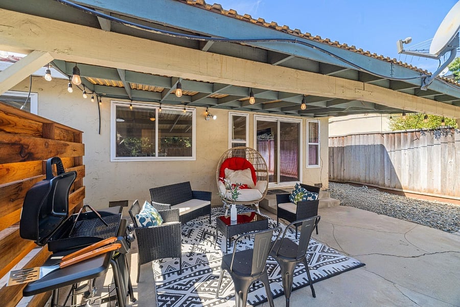 Cozy outdoor patio with covered seating, rattan furniture, glass-top table, barbecue grill, and charming string lightsideal for alfresco dining and entertaining.