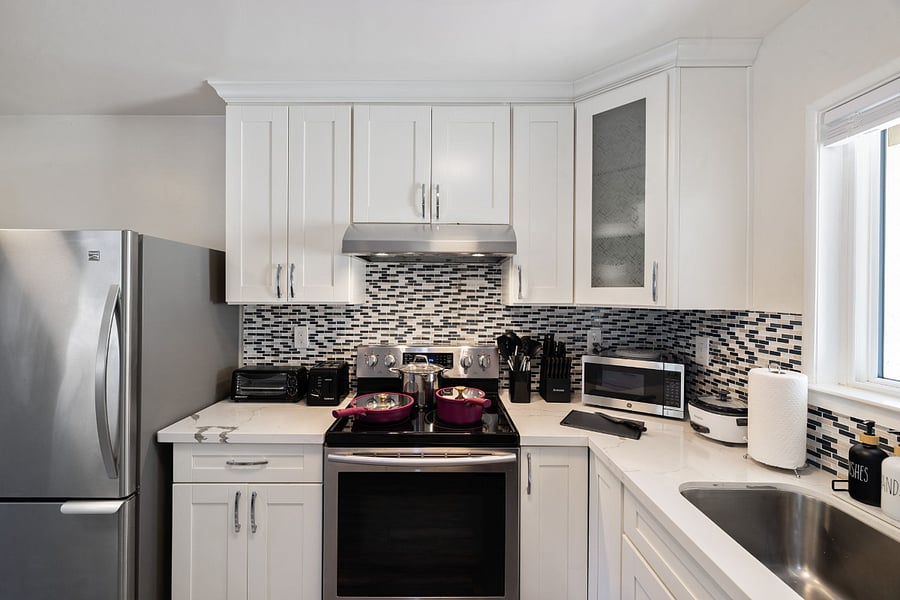 Bright, modern kitchen with white cabinets, stainless steel fridge, mosaic backsplash