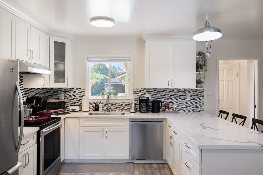 Bright modern kitchen with white cabinets, marble island, mosaic backsplash, stainless steel appliances, and barstools.