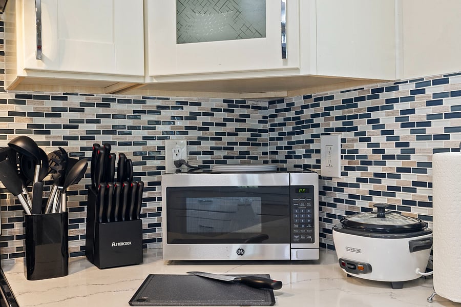 A kitchen counter with a stainless steel GE microwave, a black utensil holder with cooking tools, a black knife block with full set of knives, a white Black+Decker slow cooker, and a paper towel roll.