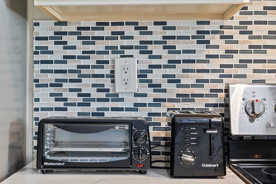 A kitchen counter with a black Elite Gourmet toaster oven and a black Cuisinart two-slice toaster against a blue, white, and beige tiled backsplash.