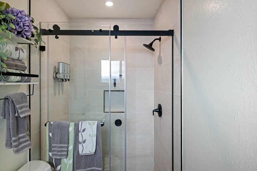 Modern bathroom with a sleek glass shower enclosure, matte black fixtures, built-in shampoo dispensers, and neatly arranged towels for your convenience and comfort.