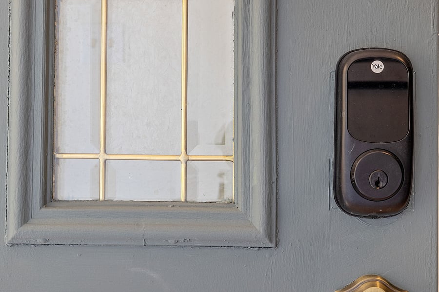 Close-up of a gray door with a decorative window and a black Yale smart lock