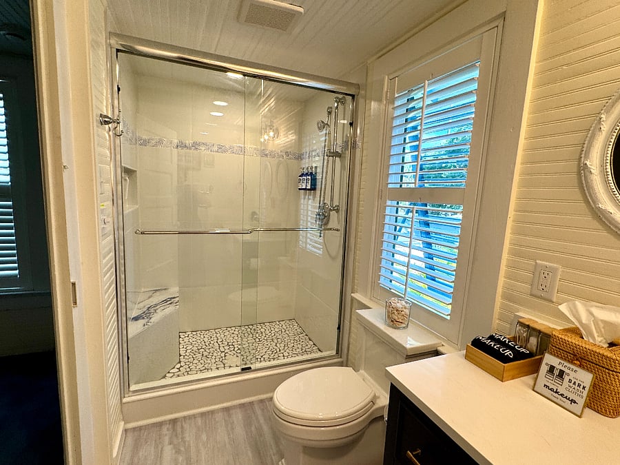 Spacious tile and stone shower with premium fixtures. glass doors, and a convenient bench.