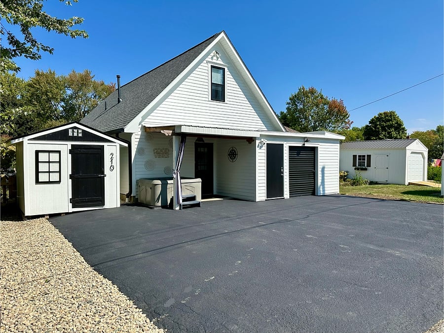 Back of home with a view of the hot tub, private parking spaces, shed with space to store personal belongings and bikes and entrance to the home.