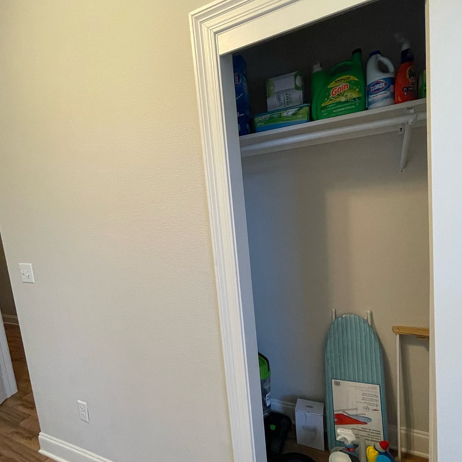 In the office closet are cleaning supplies, laundry detergent, a clothes rack, a medium-sized ironing board, and more.