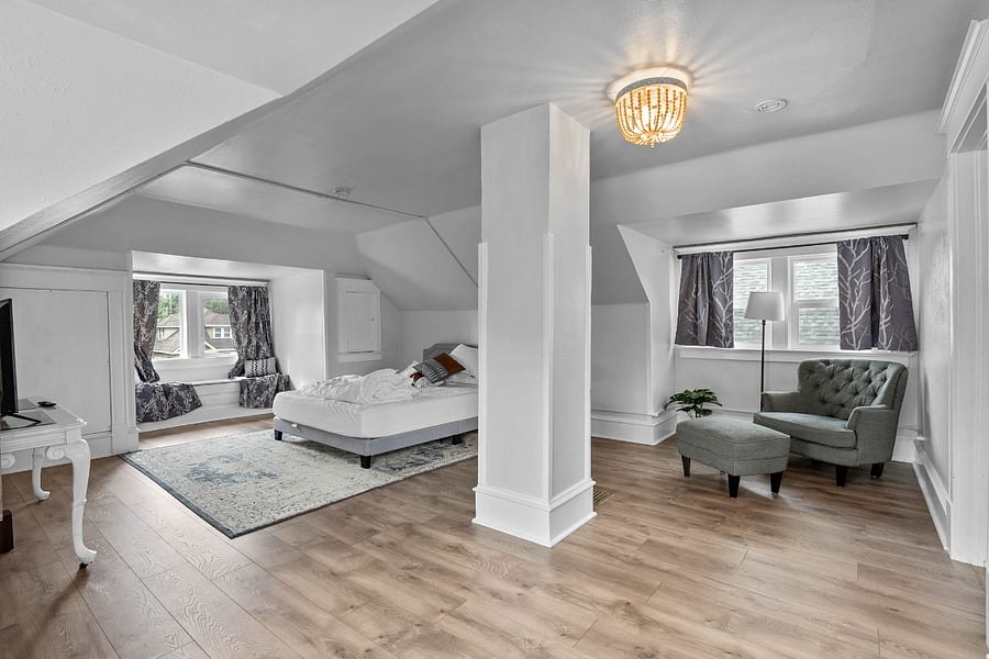 Primary bedroom with sitting area, desk, tv, window seat and queen sized bed