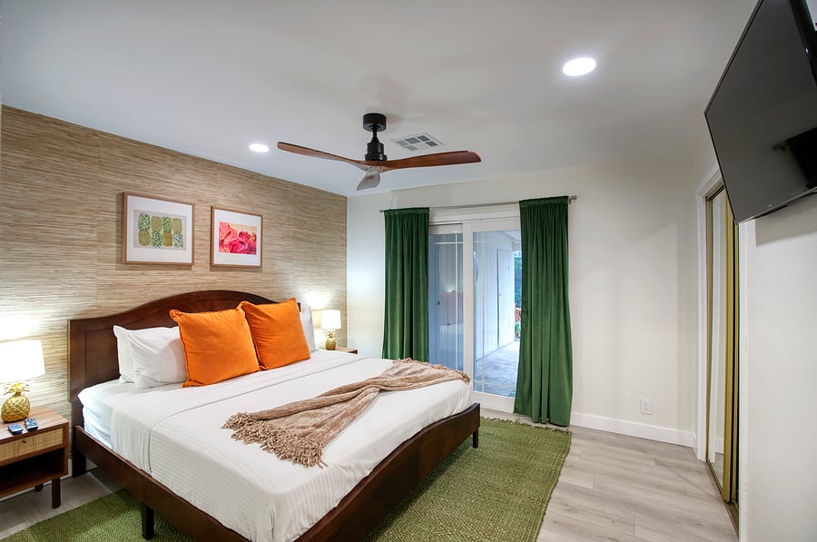 Primary suite with tropical grasscloth walls, jewel-toned pillows, and garden views for a true island retreat.