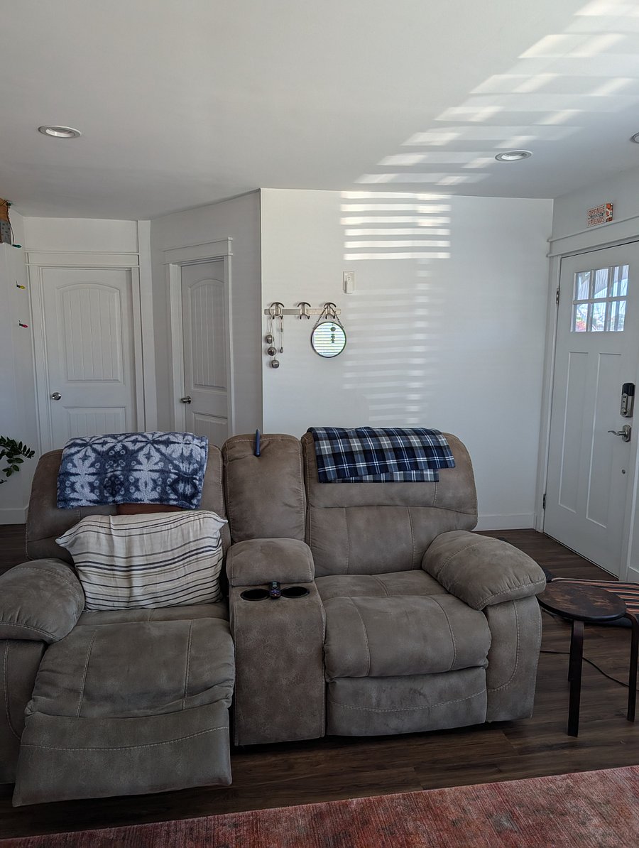 Front door on right with windows; view of living room recliner. Two room doors in view are one personal office and one bedroom that is the rental bedroom (left-most door).