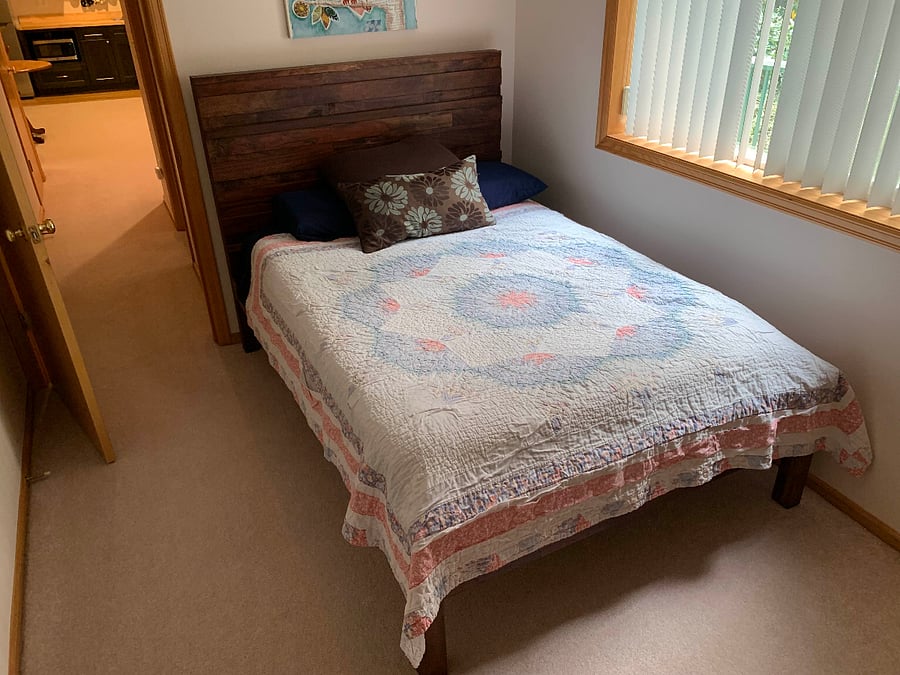 The bedroom features a full-size bed and standard closet with a window overlooking the forested creekside.
