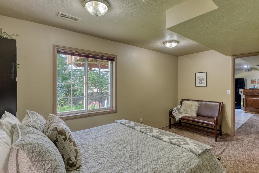 Small bedroom loveseat creates a cozy reading nook, with Sackcloth & Ashes throws, natural light, and serene views of the landscaped yard through the large window.